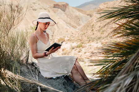 Woman reading a book wearing dress seating near to palm tree