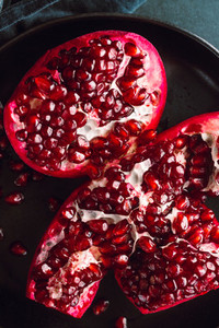 Top down view on a ripe pomegranate in a black plate on a dark background  Dark food photography