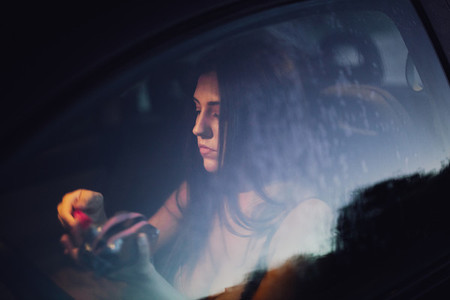 Young woman puts on makeup inside a car at sunset