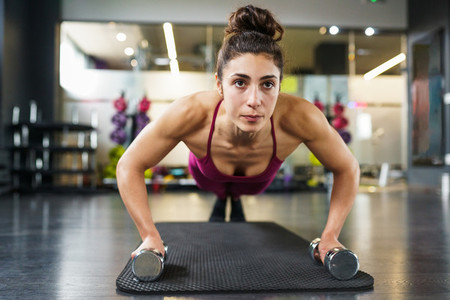 Woman doing push ups exercise with dumbbell in a fitness workout