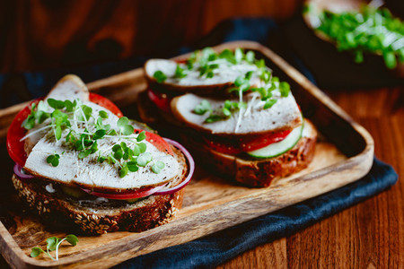 Sandwiches with turkey meat and fresh vegetables served with microgreens on a wooden plate