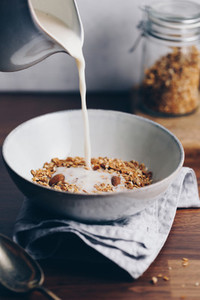Almond milk is poured in a ceramic bowl with baked granola Healthy vegetarian breakfast