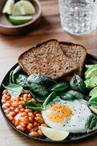 Healthy breakfast or lunch at home or cafe with fried egg  avocado  toasts  beans and fresh spinach on a wooden table
