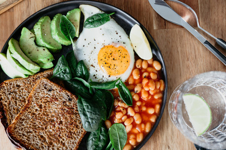 Healthy breakfast or lunch at home or cafe with fried egg avocado toasts beans and fresh spinach on a wooden table