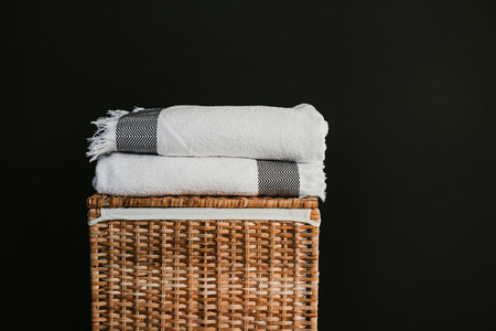 White cotton towels on a rattan box against black wall in a laundry