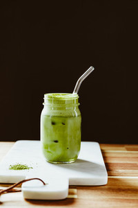 Matcha green tea latte in a glass jar with glass tube on a white marble tray  Healthy clean eating concept