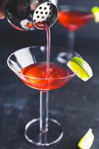 Pouring red cocktail with lime in Martini glass on a table