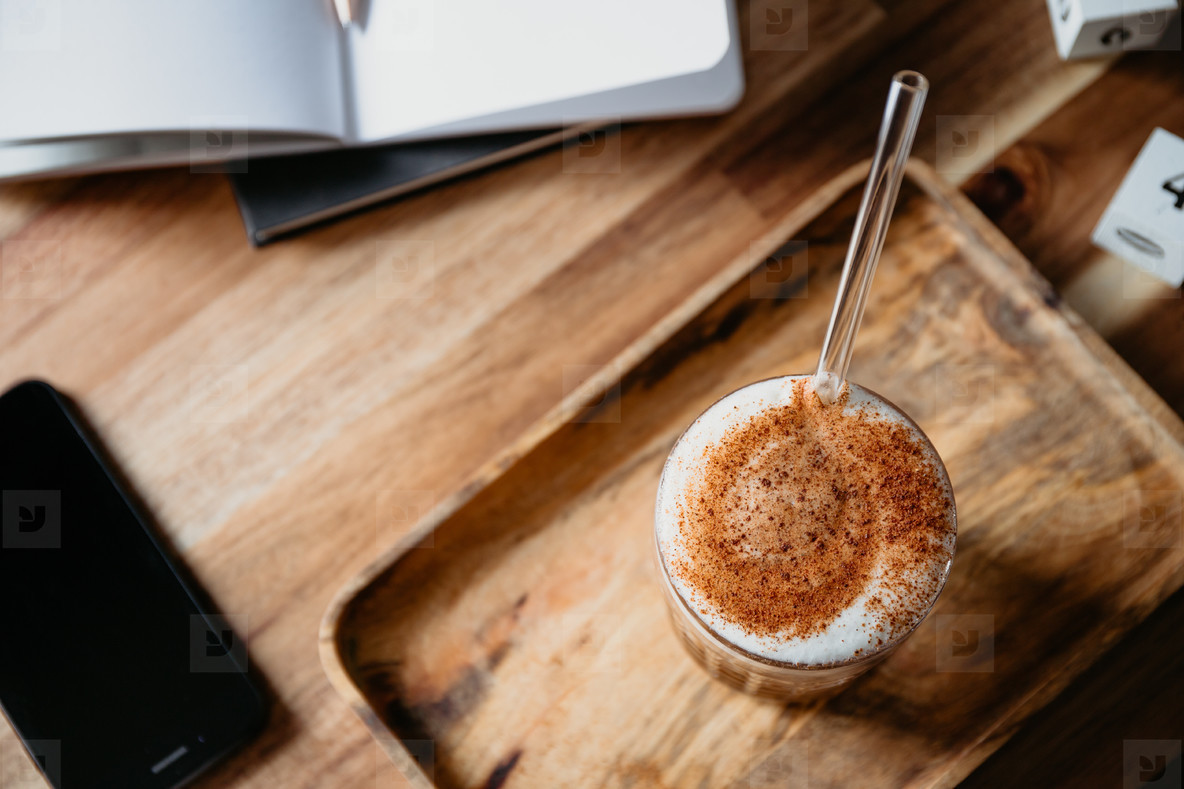 Cup of latte served with glass tube on a wooden work desk Coffee break concept
