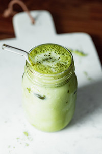 Matcha green tea latte in a glass jar with glass tube on a white marble tray  Healthy clean eating concept