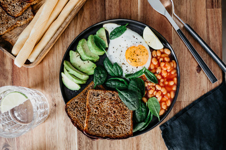 Healthy breakfast or lunch with fried egg  avocado  toasts  beans and fresh spinach on a wooden table