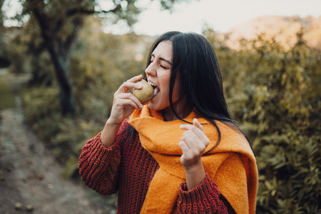 Young woman biting a pear in the field wearing a sweater