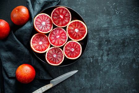 Cutted blood oranges in a plate on a dark black background  Top view  flat lay composition  copy space