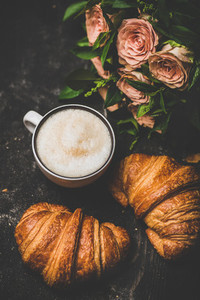 Cup of cappuccino fresh croissants and bouquet of pink flowers