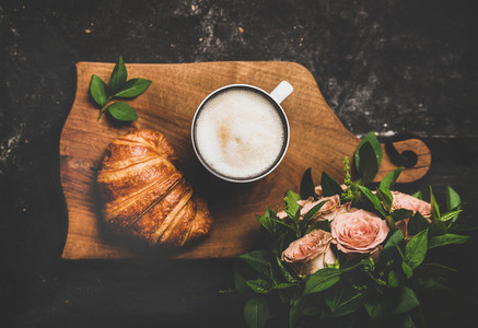 Cup of cappuccino  croissant and pink flowers over black background