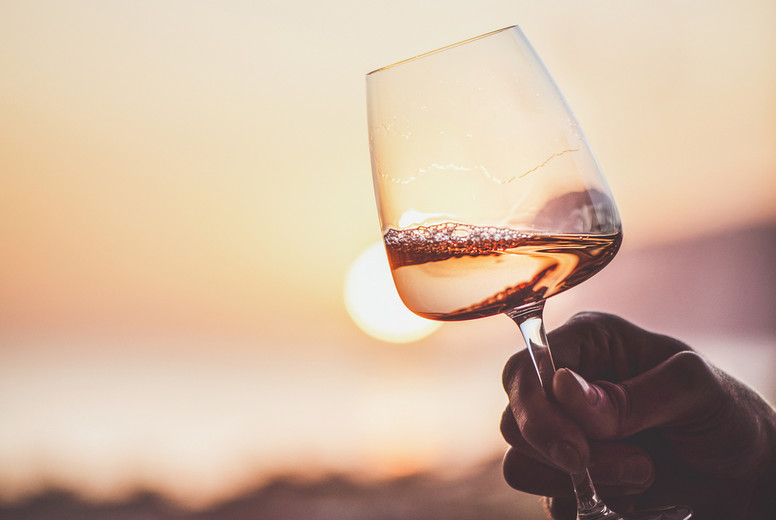 Rose wine in hand with sunset and sea at background