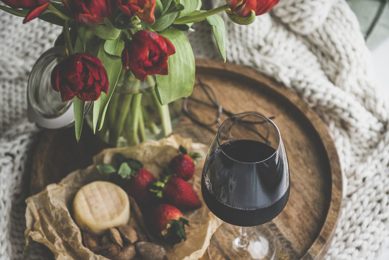 Glass of red wine, snacks and tulips on wooden board