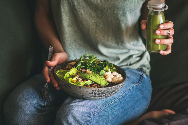 Woman sitting and holding healthy superbowl and smoothie