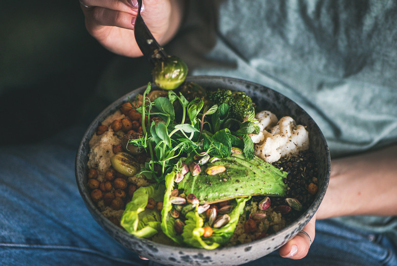 Woman sitting and eating healthy vegan dish from bowl