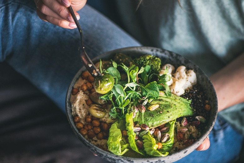Woman sitting and eating vegan dish with himmus and avocado