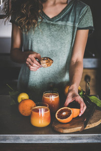 Woman making fresh blood orange juice or smoothie in kitchen
