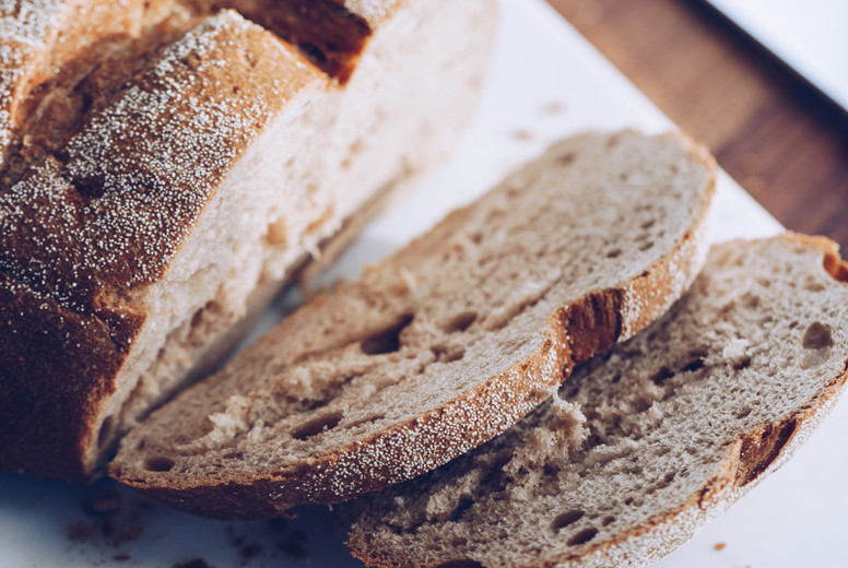 Cutting rye bread loaf and a knife on a white marble cutting board.