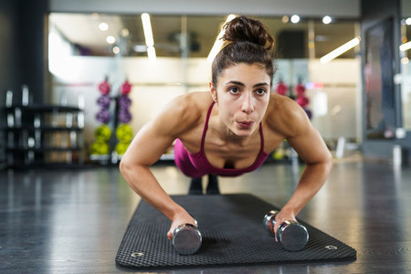 Woman doing push ups exercise with dumbbell in a fitness workout