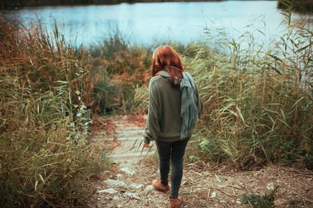 Young redhead woman walking to the lake shore with headphones