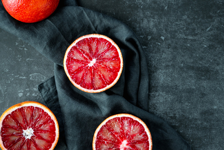 Flat lay food composition with blood oranges on a dark blue background.