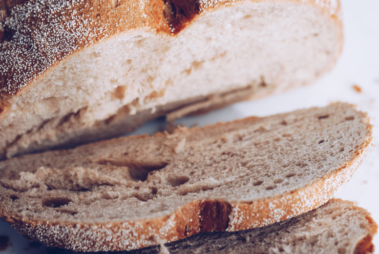 Cutted rye bread loaf and a knife on a white marble cutting board.