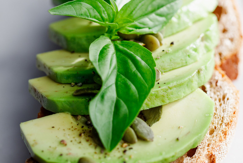 Avocado toast with pepitas and fresh basil on a white marble cutting board. Home cooking, healthy eating concept.