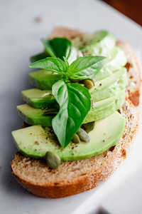 Avocado toast with pepitas and fresh basil on a white marble cutting board  Home cooking  healthy eating concept