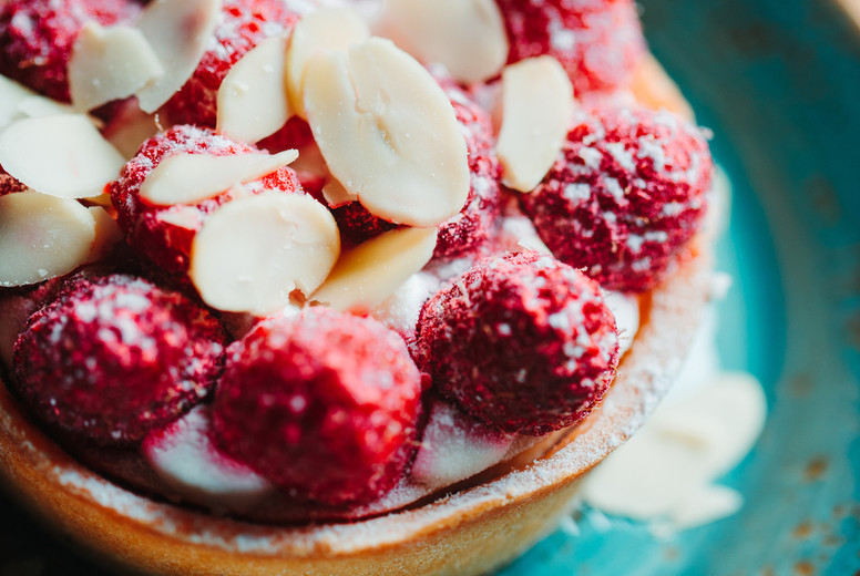 Raspberry tartlet dessert with almond flakes on a blue ceramic plate. Close-up view.