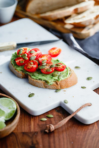 Avocado toast with cherry tomatoes and pepitas on a white marble cutting board  Home cooking  healthy eating concept