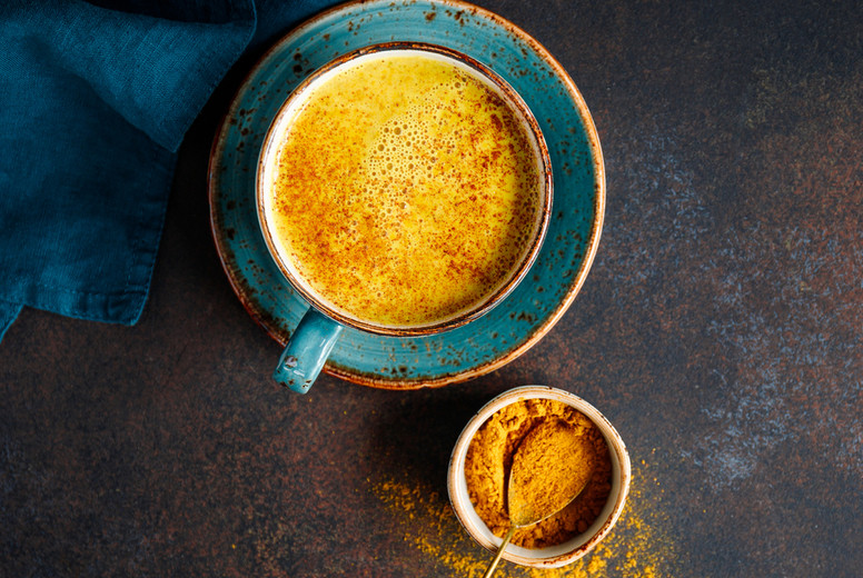 Top down view of turmeric latte cup on a textured dark background.