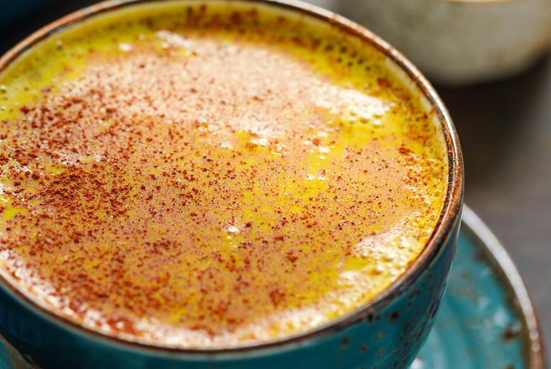 Closeup view of turmeric latte cup on a textured dark background.