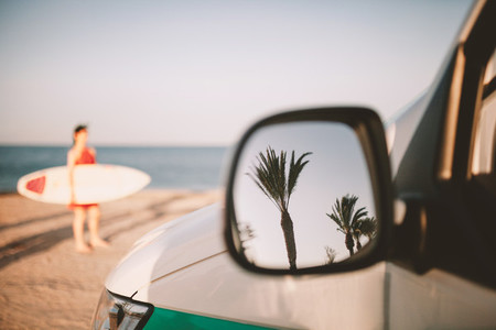 Reflection of palm trees in van outside mirror on the beach