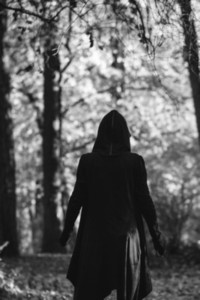 View from the back on a black witch in a mantle during ritual in a forest  Black and white moody photography  The concept of Halloween and witchcraft