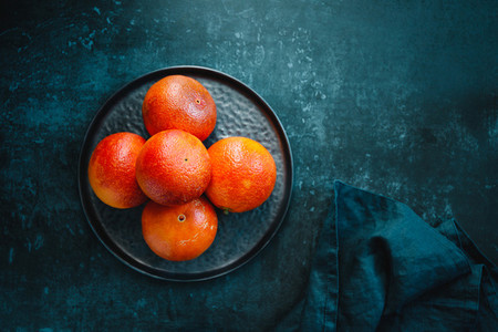 Blood oranges in a plate on a dark blue background Top view