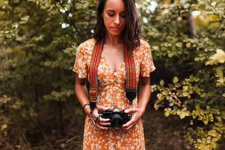 Young woman with analog camera wearing a dress in the forest