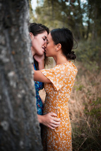Two women kissing in the woods with dresses