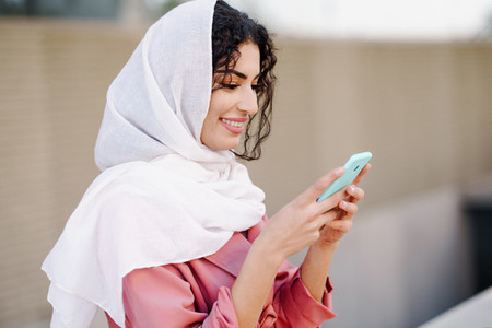 Young Muslim woman wearing hijab texting message with her smartphone
