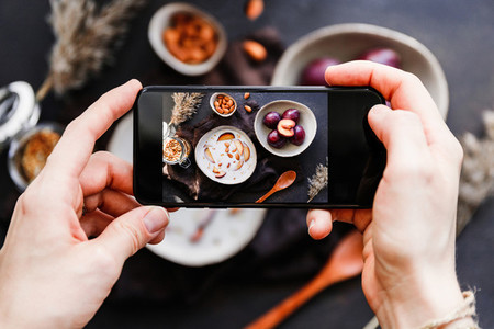 Hands hold smartphone and take picture of morning porridge with almond and sliced plum Food photography concept