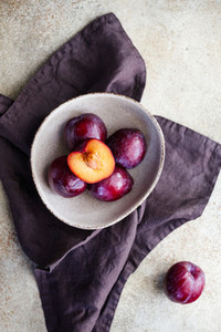 Top view of purple plum in a ceramic bowl on a beige textured background