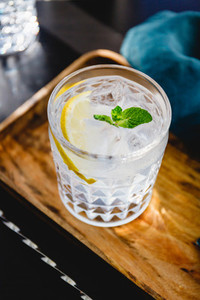 Refreshing cold summer cocktail with soda water lemon and ice cubes on a wooden tray