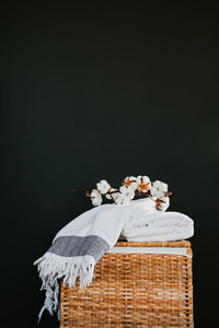 White cotton towels on a rattan box with cooton branch against black wall in a laundry