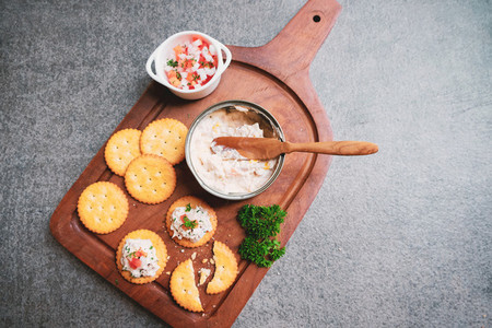 Top view of tasty tuna spread with crackers on wooden tray and b