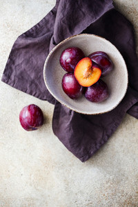 Top view of purple plum in a ceramic bowl on a beige textured background