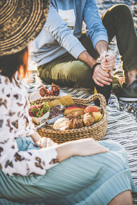 Young couple opening bottle of sparkling wine at summer picnic