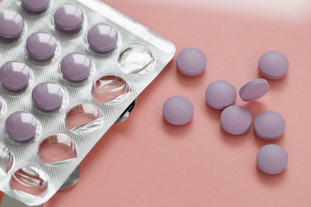 Close up of purple pills in a pack on a pink background