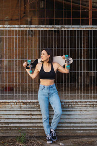 Young woman skater smiling holding her longboard behind her head